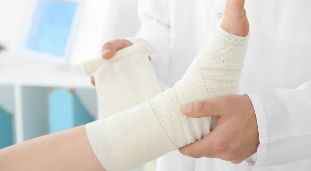 【足関節捻挫】の怪我にて、足関節周辺の【靭帯】を痛めてしまい、専門家に包帯を巻いてしっかりと固定してもらっている状況です。捻挫などの怪我による痛みや不安を抱えつつも、迅速で丁寧な処置を受けてホッと安心している場面です。